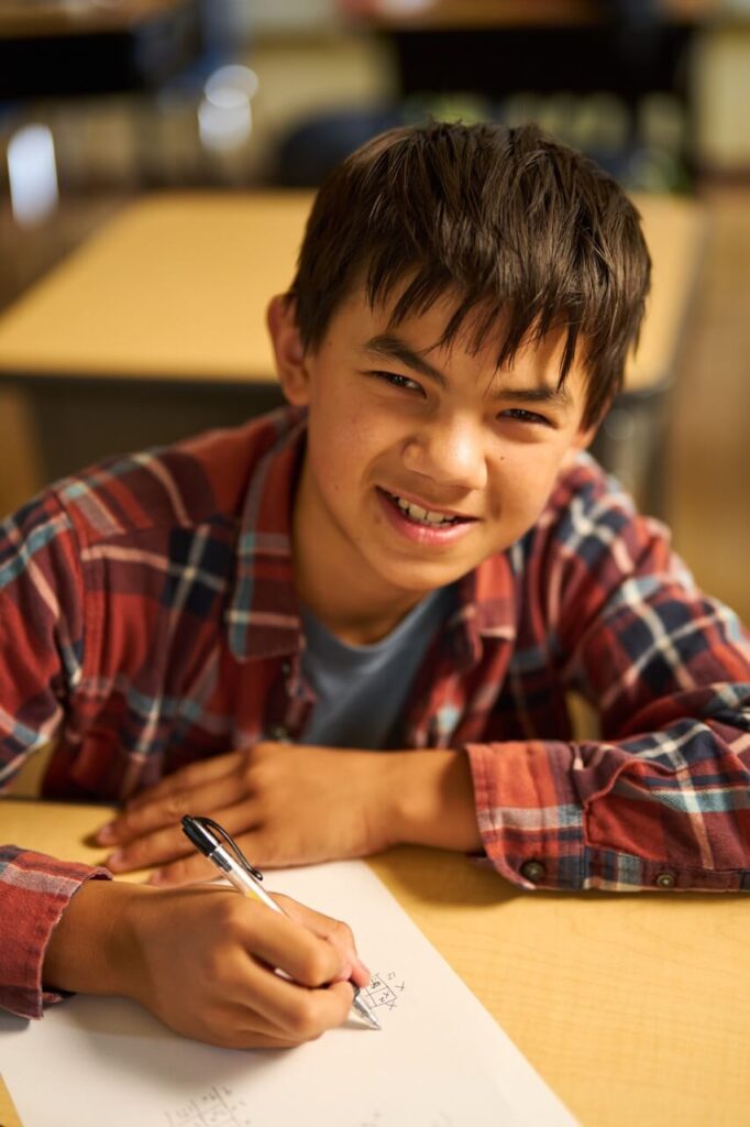 A middle school boy smiles while he works on a math problem.