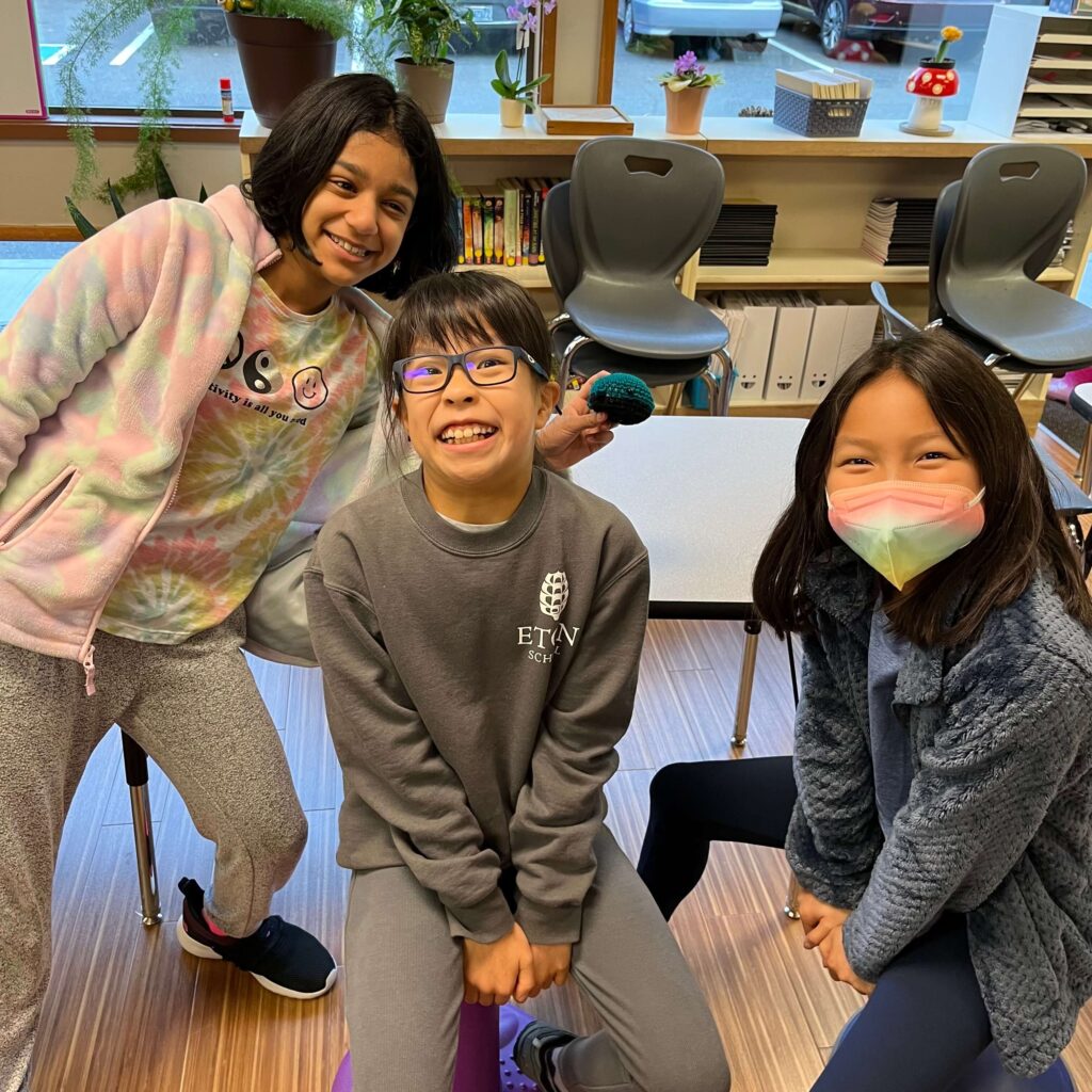 Three elementary students smile together in a classroom.