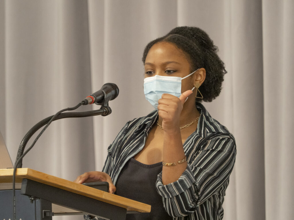 A high school student in a facemask speaks into a microphone.